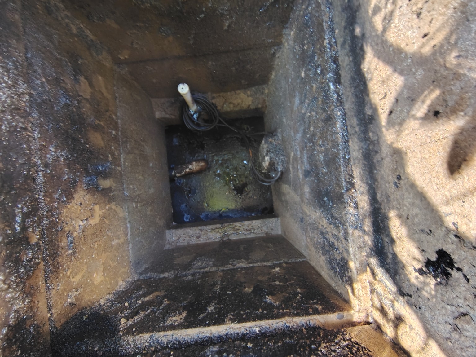 Wide inspection view inside the pump chamber showing piping, wiring and accumulated residue